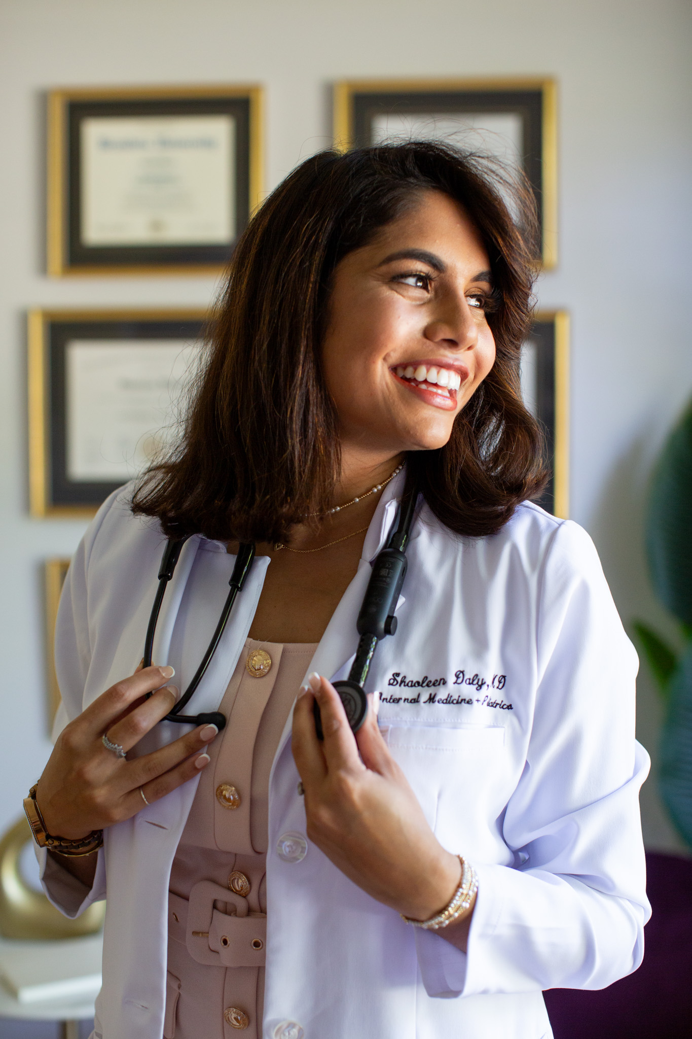 Dr. Daly smiling in her white coat with framed credentials behind her