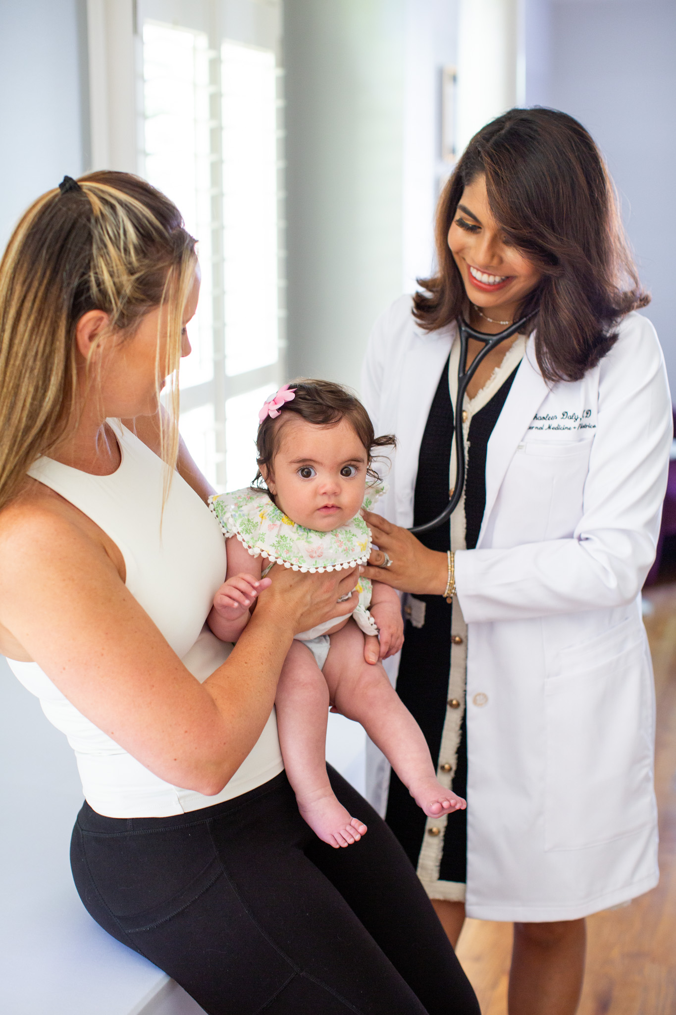 Dr. Shaoleen Daly listening to an infant’s heartbeat while the baby sits with her mother